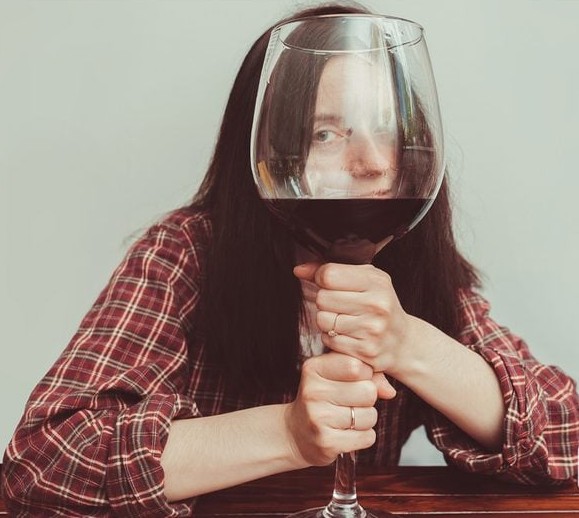 Osoba držiaca obrovský pohár červeného vína, čiastočne odhalená za sklom.