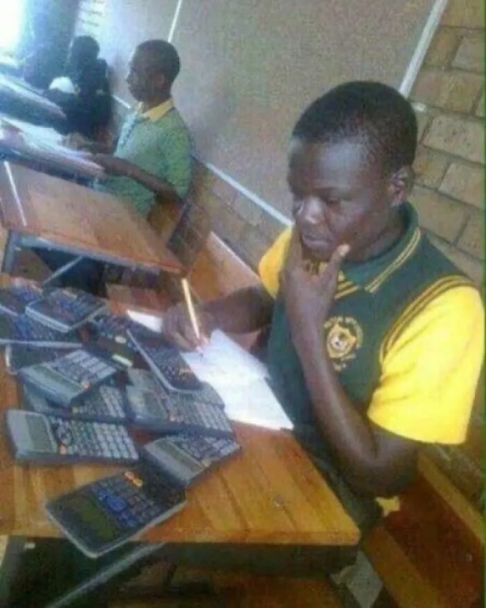 Študent s viacerými kalkulačkami rieši zložitý matematický príklad v triede.