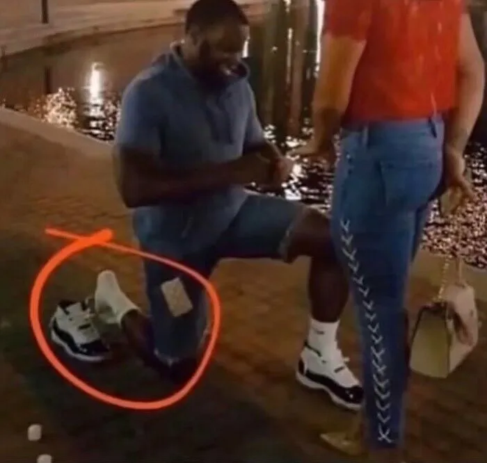 Muž kľačiaci pri vode počas zásnubného momentu s topánkou vedľa jeho nohy v ponožke.