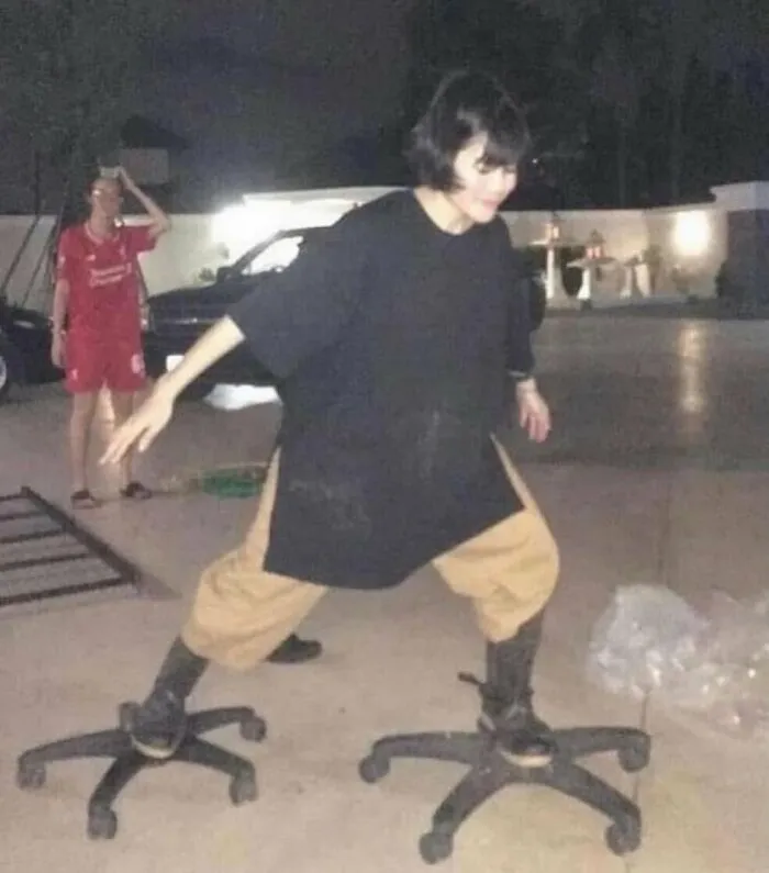 Osoba balancuje na dvoch kancelárskych stoličkách vonku v noci, pričom sa snaží udržať rovnováhu.