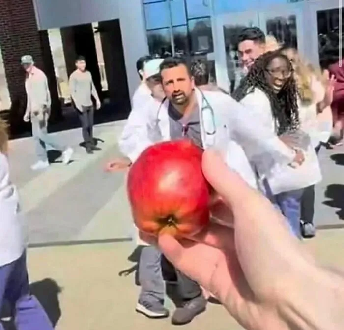 Držanie jablka pred skupinou ľudí v bielych plášťoch na ulici.