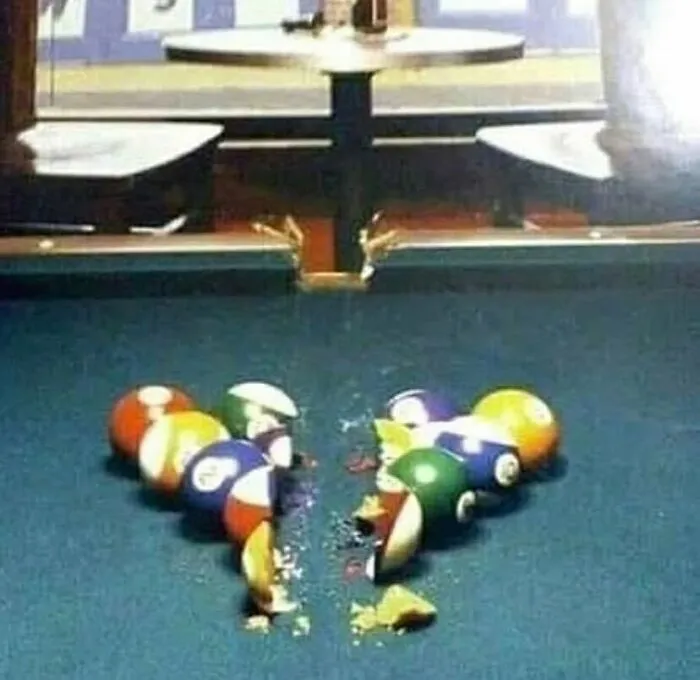 Rozbité biliardové gule na stole v kombinácii s lámacím kolíkom, symbolizujúce zlyhanie alebo chaos v hre.