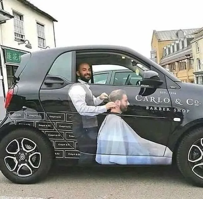 Auto s kreatívnou reklamou na holičstvo, ktoré vytvára ilúziu holenia zákazníka priamo vo vozidle.