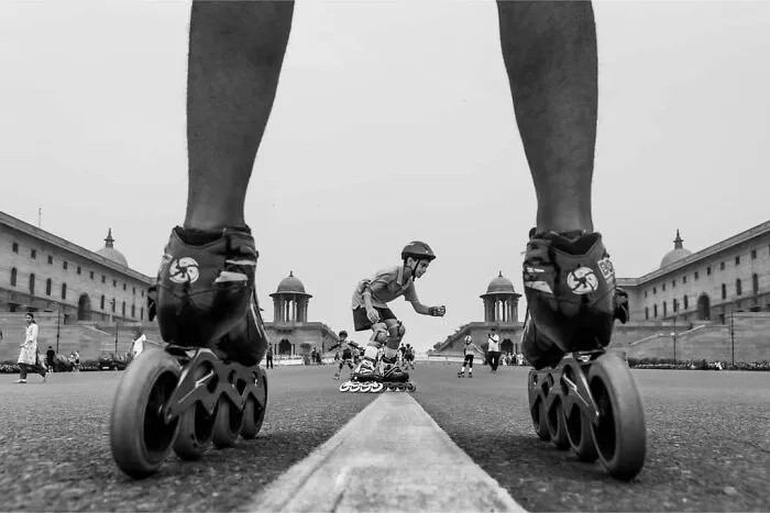 Inline korčuliar v akcii na širokej ulici medzi historickými budovami, pozorovaný z pohľadu cez obrovské kolieskové korčule.