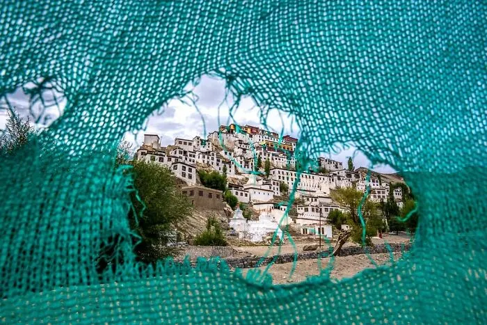 Výhľad na skalnatú dedinu cez otvor v modrej tkanine, obklopenú prírodou a mestskými budovami v pozadí.