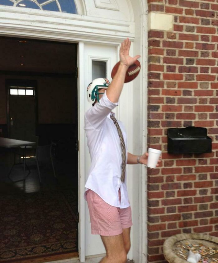 Muž v prilbe chytá loptu pri dverách, oblečený v košeli a šortkách, s kávovým pohárom v ruke.