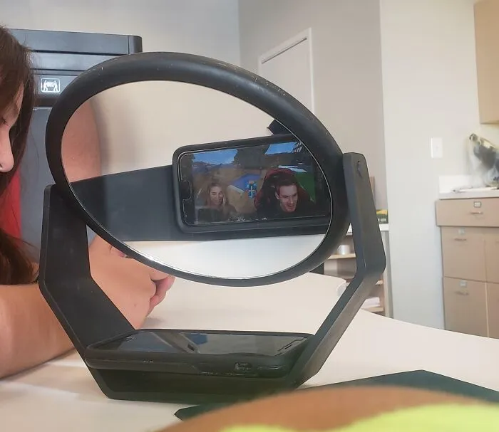 Osoba pozerajúca video na mobile, odraz v kruhovom stojane na stole v kancelárii.