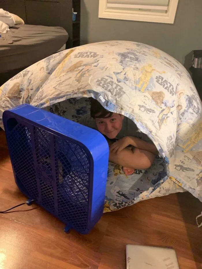 Dieťa sa hrá pod prikrývkou vytvárajúc fort s ventilátorom v miestnosti.