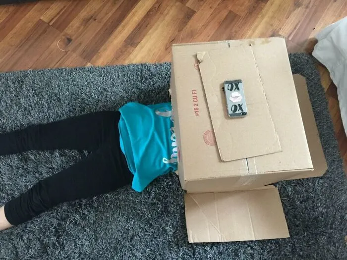 Detská hra s použitím veľkej kartónovej škatule s páskou na koberci v obývačke, kreatívne skrývanie.