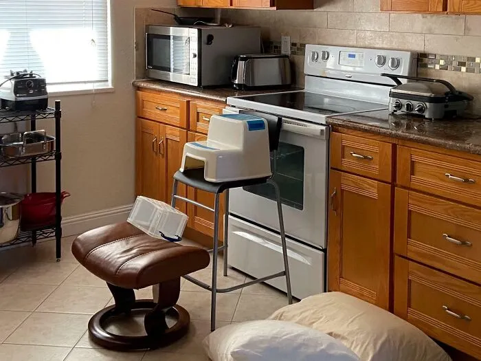 Kuchyňa s pecou, mikrovlnkou a toasterom, pri rúre stolička s malým spotrebičom na vrchu.