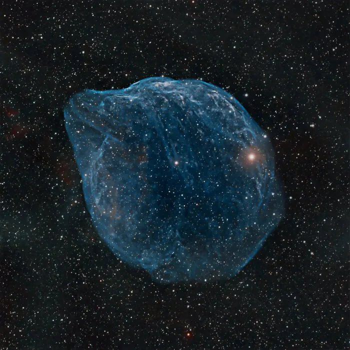 Modrá hmlovina v tvare bubliny obklopená hviezdnym poľom na nočnej oblohe vesmíru.