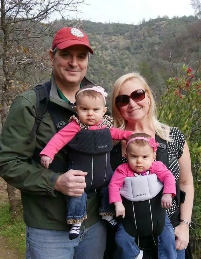 Rodinný výlet v prírode s dvojčatami v nosičoch, všetci v pohode a spokojní.