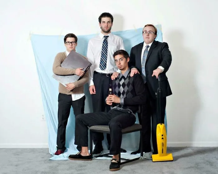 Štyria muži v neformálnom oblečení a oblekoch pózujú v miestnosti, jeden sedí, ostatní stoja.