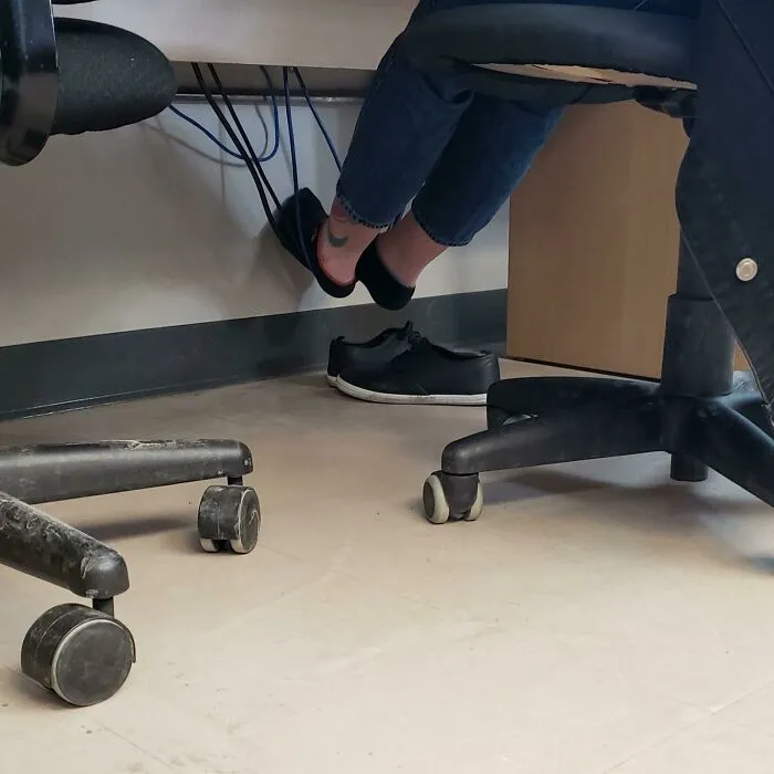 Osoba sedí na kancelárskej stoličke s chodidlami na železnej tyči pod stolom v kancelárskom prostredí.