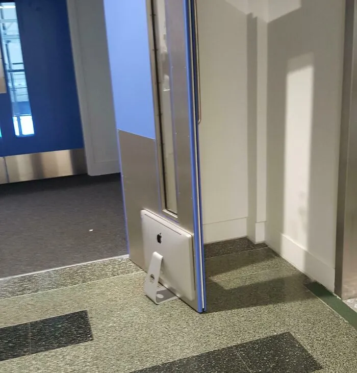 Počítač Apple zachytený vo dverách ako netradičný spôsob ich udržania otvorených na verejnom mieste.