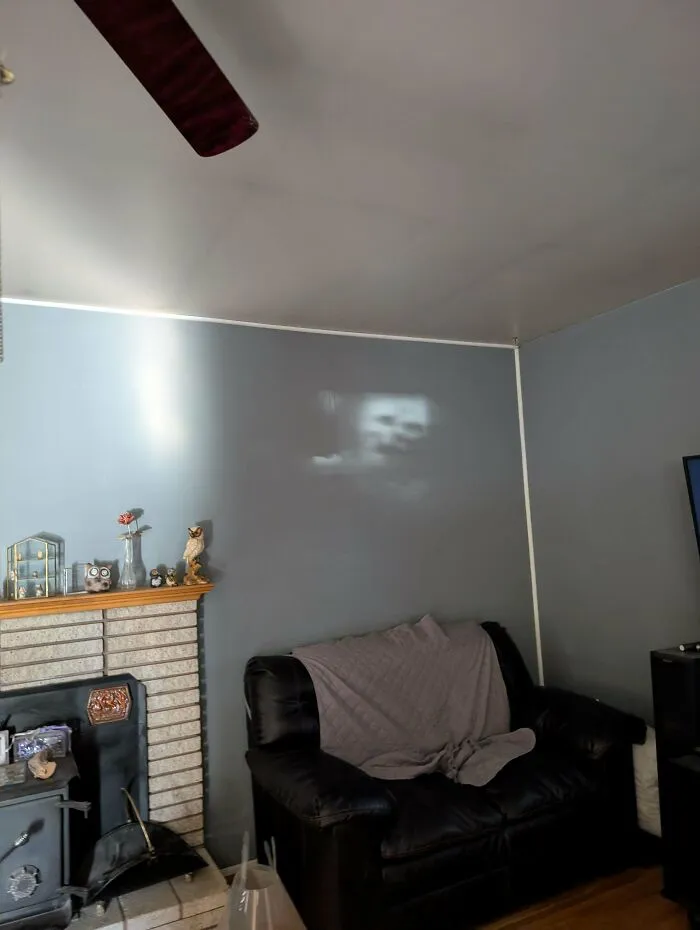 Obývačka s koženou sedačkou, krbom so soškami na polici a rozmazaným obrazom premietaným na stene.