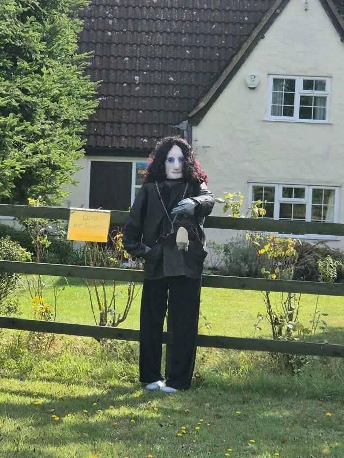 Strašidelná figurína na záhrade pred domom s tabuľkou „Gone not forgotten“.