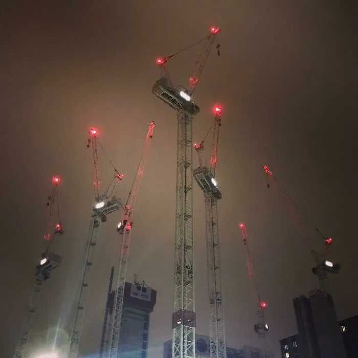 Žeriavy osvetlené červenými svetielkami na nočnej oblohe v meste, symbolizujúce rozvoj a výstavbu.