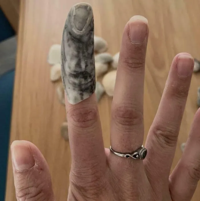 Ruka s prstom, na ktorom je kameň tvarom pripomínajúci necht, na drevenom povrchu.