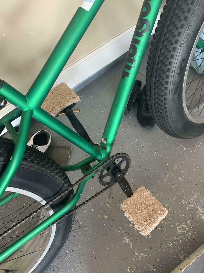 Zelený bicykel s pedálmi obalenými v koberci, odstavený na podlahe v garáži.