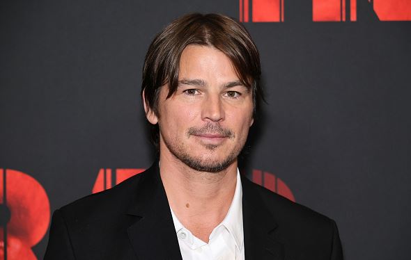 Osoba v obleku na červenom koberci s čiernym pozadím, promo akcia alebo filmová premiéra.