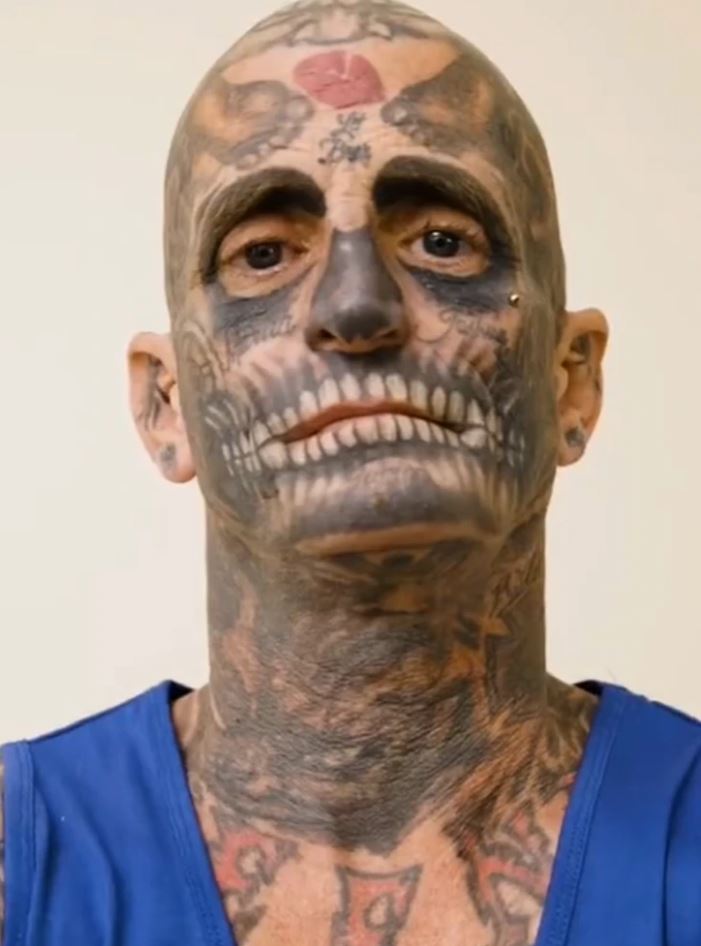 Muž s rozsiahlymi tetovaniami tváre a krku v modrom tielku.