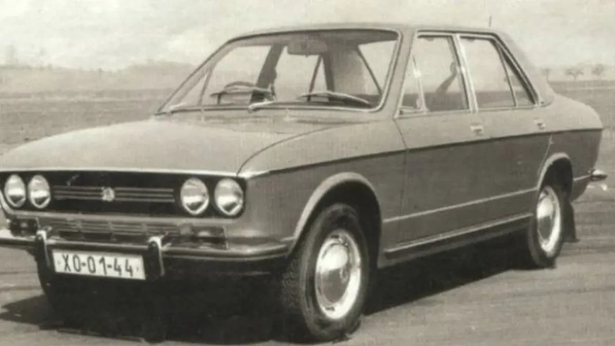 Starý model sedanu na vidieckej ceste v čiernobielej fotografii.