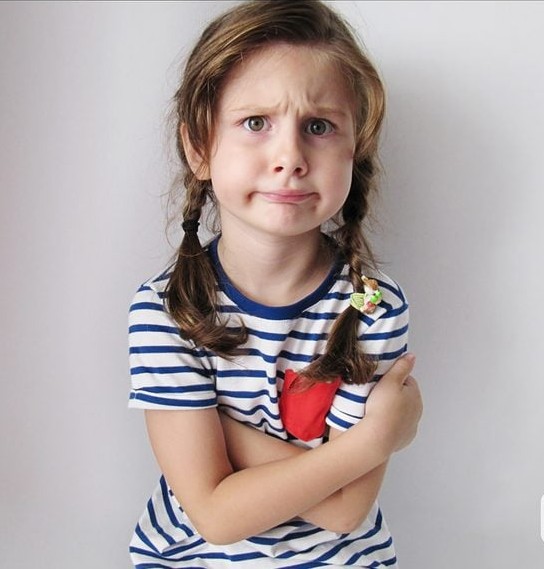 Dievčatko v pruhovanom tričku s vrkočmi a zamysleným výrazom.