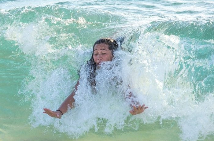 Osoba sa usmieva, ponorená vo vlnách na pláži, užívajúc si letné osvieženie.