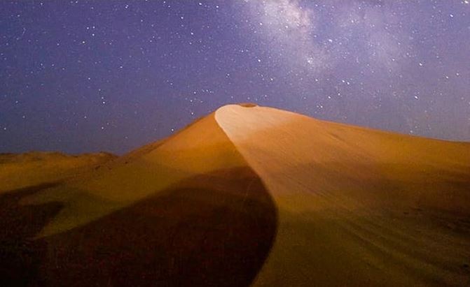 Piesočná duna pod hviezdnatou oblohou. Nočné ticho púšte zvýraznené Mliečnou cestou na oblohe.