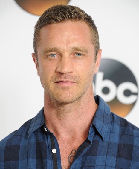 Muž v kockovanej košeli pred logom spoločnosti na bielom pozadí.