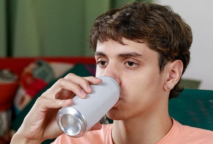 Osoba pije z plechovky v pohodlnom domácom prostredí.