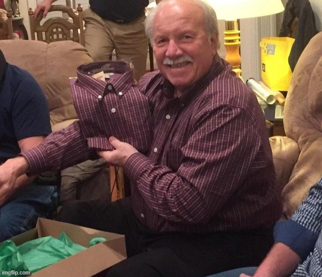 Starší muž s darovanou košeľou, ktorá zodpovedá jeho oblečeniu, vo veselej domácej atmosfére.