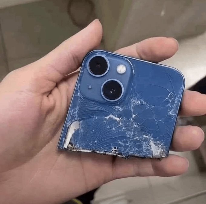 Rozbitý modrý smartfón s poškodeným zadným krytom a kamerou v ľudskej ruke.