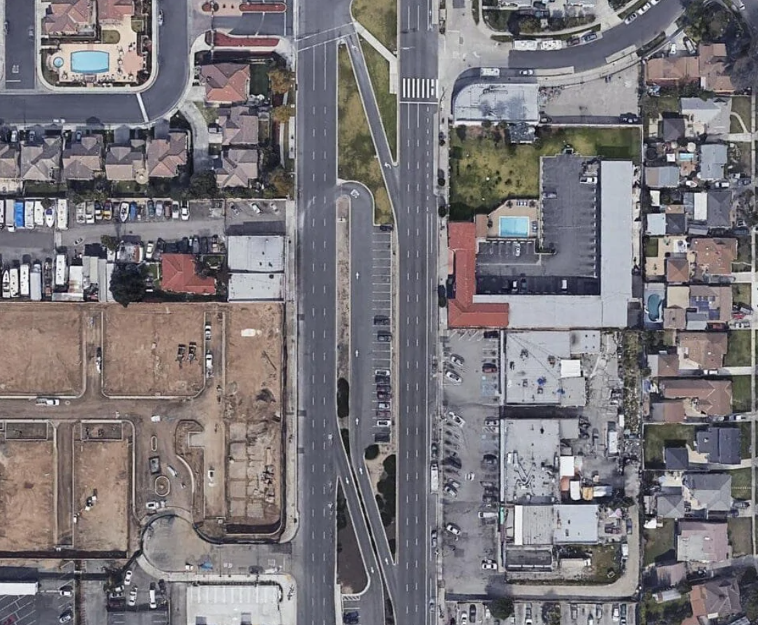 Letecká snímka mestského mesta s obytnými domami, bazénmi, a hlavnou cestou uprostred.