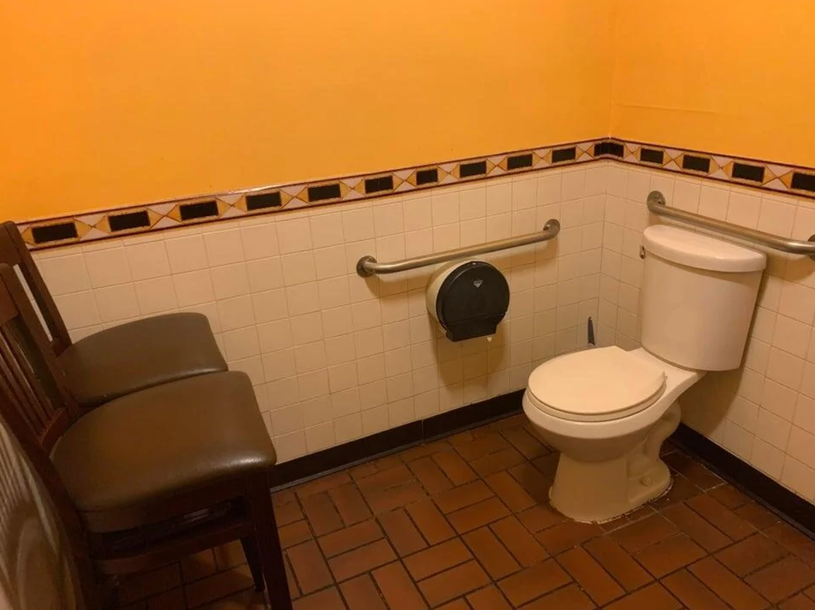 Toaleta s oranžovými stenami a dvomi stoličkami vedľa WC.