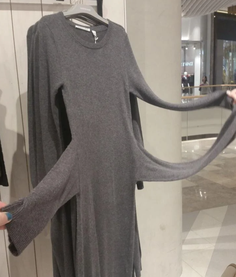 Šedé šaty na ramienku v obchode, s nadmerne dlhými rukávmi, roztiahnutými v priestore.