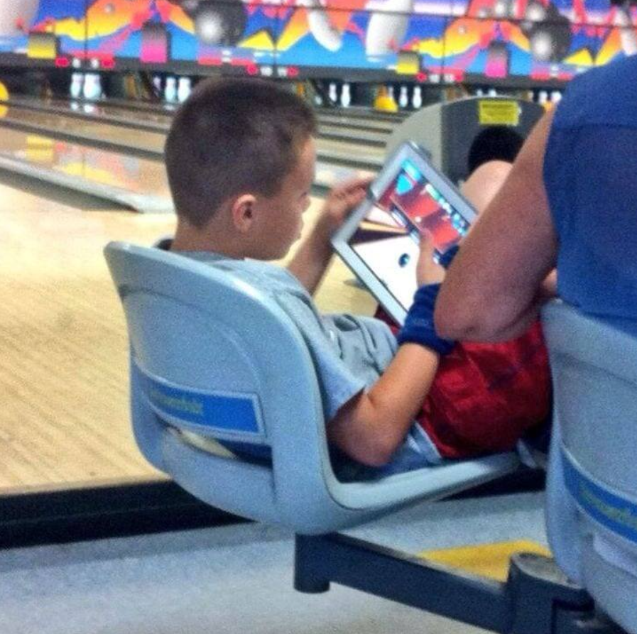 Chlapec na tabletke hrá digitálnu bowlingovú hru v bowlingovej hale.