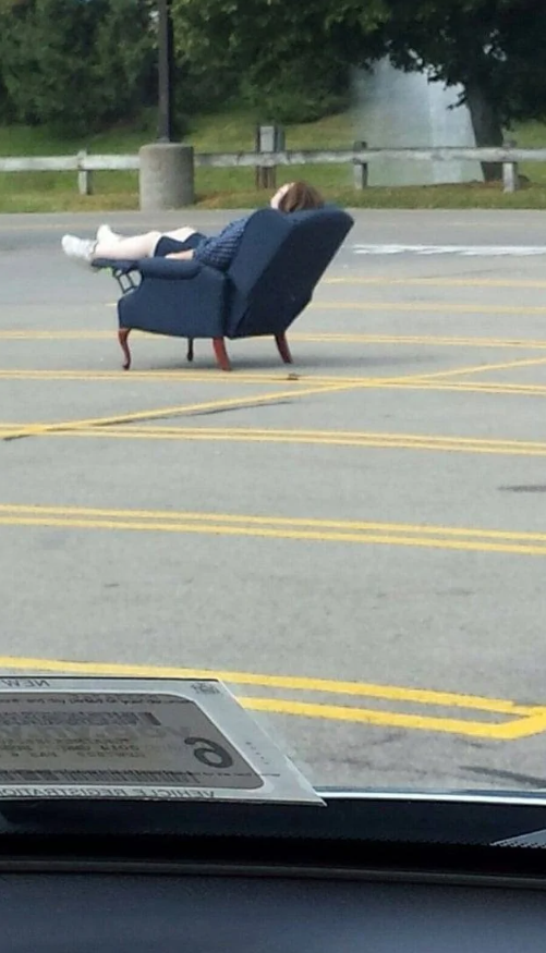 Osoba relaxuje na kresle uprostred prázdneho parkoviska pod holým nebom.