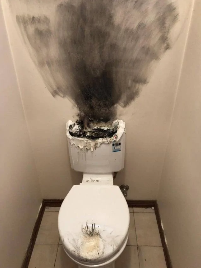 Znečistená toaleta so sadzami a poškodenými stenami po požiari alebo výbuchu, biely interiér.