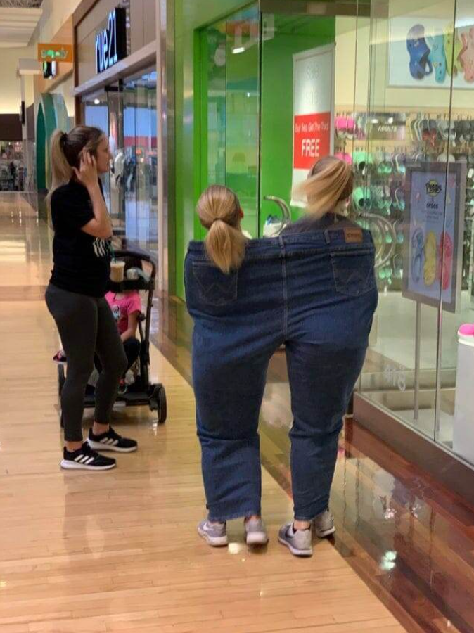 Dve osoby v nákupnom centre zdieľajú jedny veľké džínsy, ako zábavný módny výstrelok.