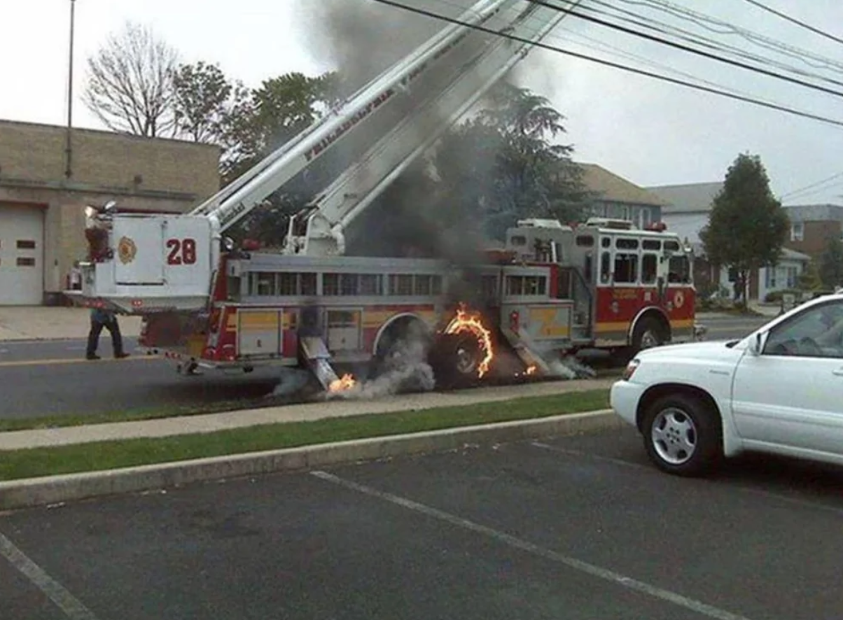 Požiarnický voz na ceste s horiacim kolesom, z ktorého uniká dym.