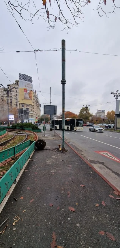 Mestská ulica s autobusom, budovami a jesennými stromami v pozadí za oblačného dňa.