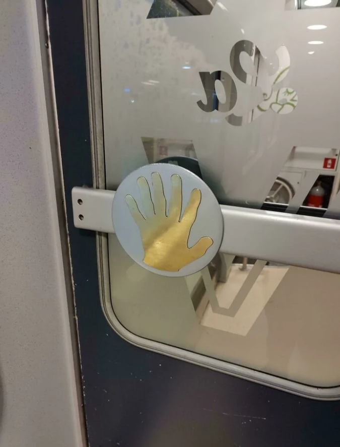 Nálepka ruky na automatických dverách vlaku, naznačujúca miesto na dotyk pre otvorenie.