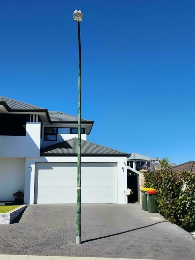 Lampa na stĺpe pred dvojgarážou moderného domu za slnečného dňa.