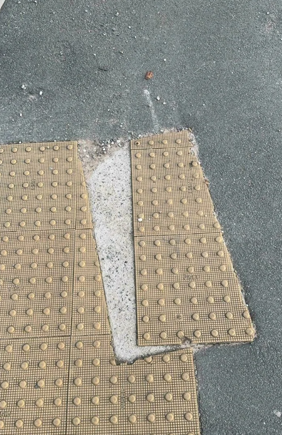 Nezosúladené plastové dlaždičky na chodníku s viditeľným poškodením betónu.