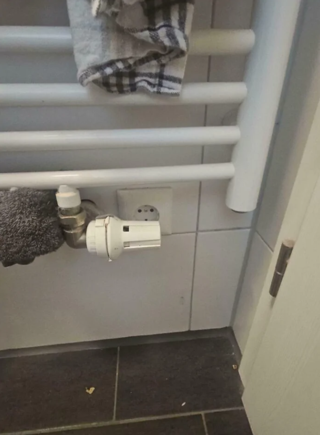 Radiátor s uterákmi a termostatickým ventilom v kúpeľni. Napájacia zásuvka blízko radiátora.