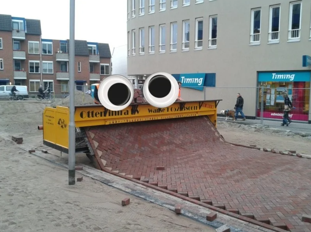 Stroj na pokladanie dlažby v meste, pripomínajúci tvár s veľkými očami, kladie cestu z tehlových blokov.