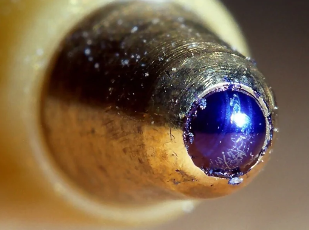 Detail hrotu guľôčkového pera s modrým atramentom, makro pohľad.