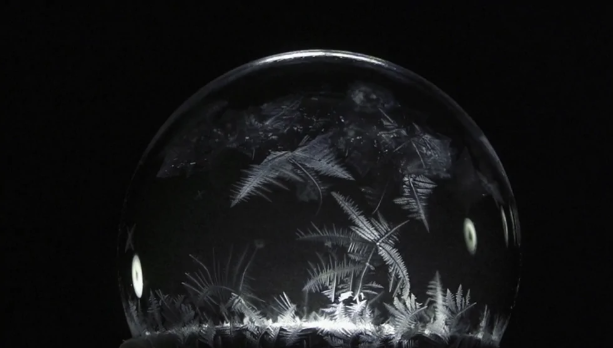 Zamrznutá mydlová bublina s jemnými kryštálmi v zime, čierne pozadie.